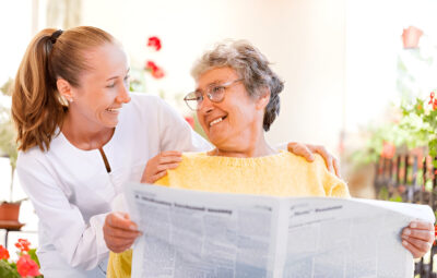 Blog 3 duas mulheres conversando felizes, uma com um jornal nas mãos, ambas contentes com a eficácia da calcinha absorvente retex.